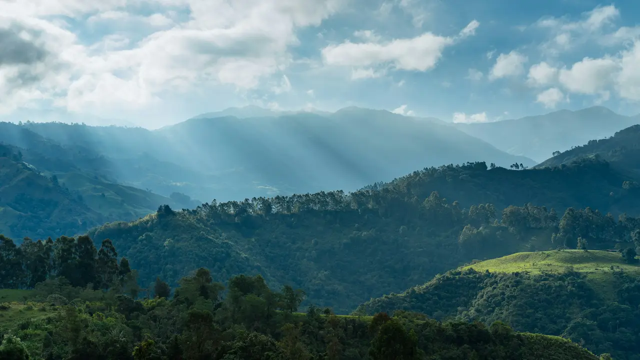 Montañas verdes con rayos de sol que atraviesan las nubes
