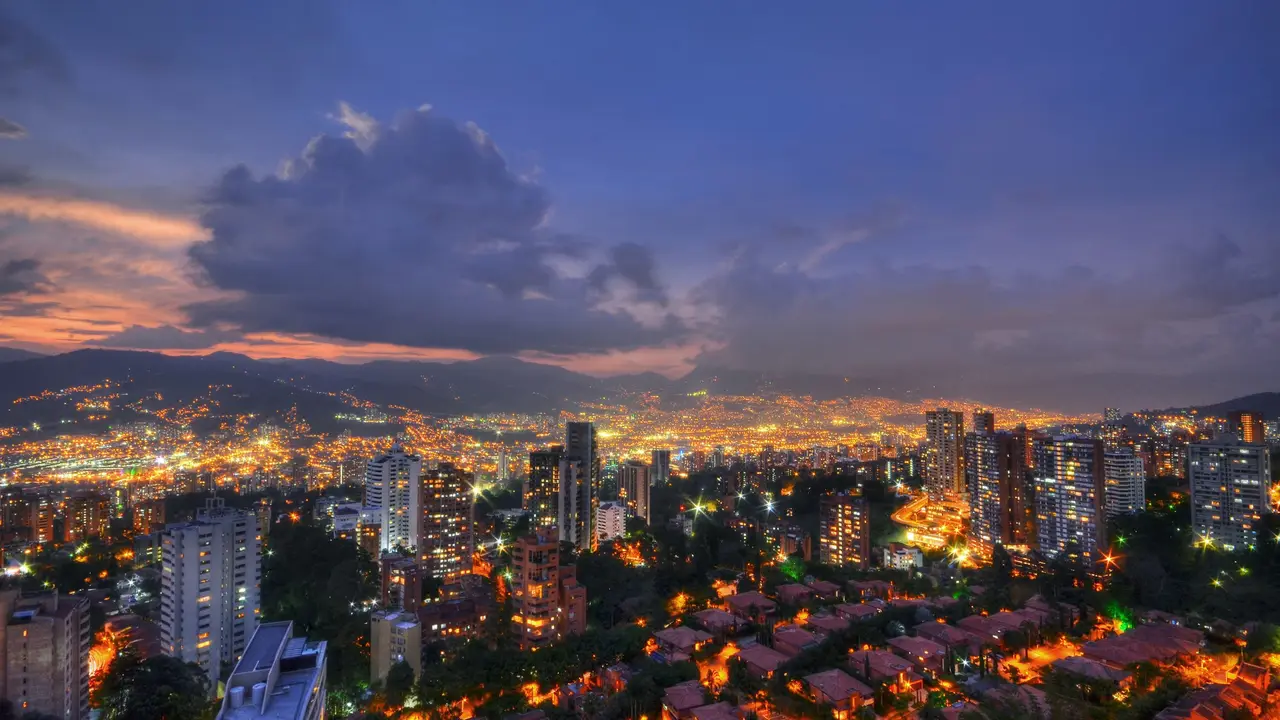 Medellín al anochecer, con las luces de la ciudad encendidas bajo un cielo violeta