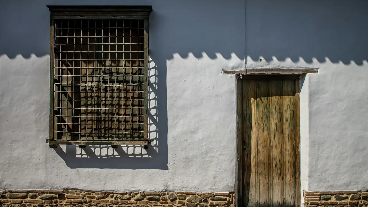 Fachada colonial blanca con ventana de reja y puerta de madera