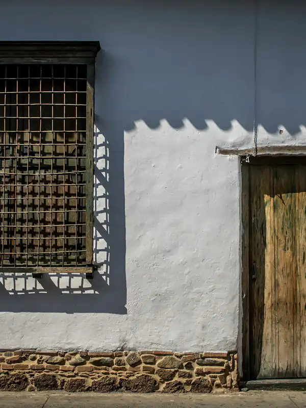 Fachada colonial blanca con ventana de reja y puerta de madera